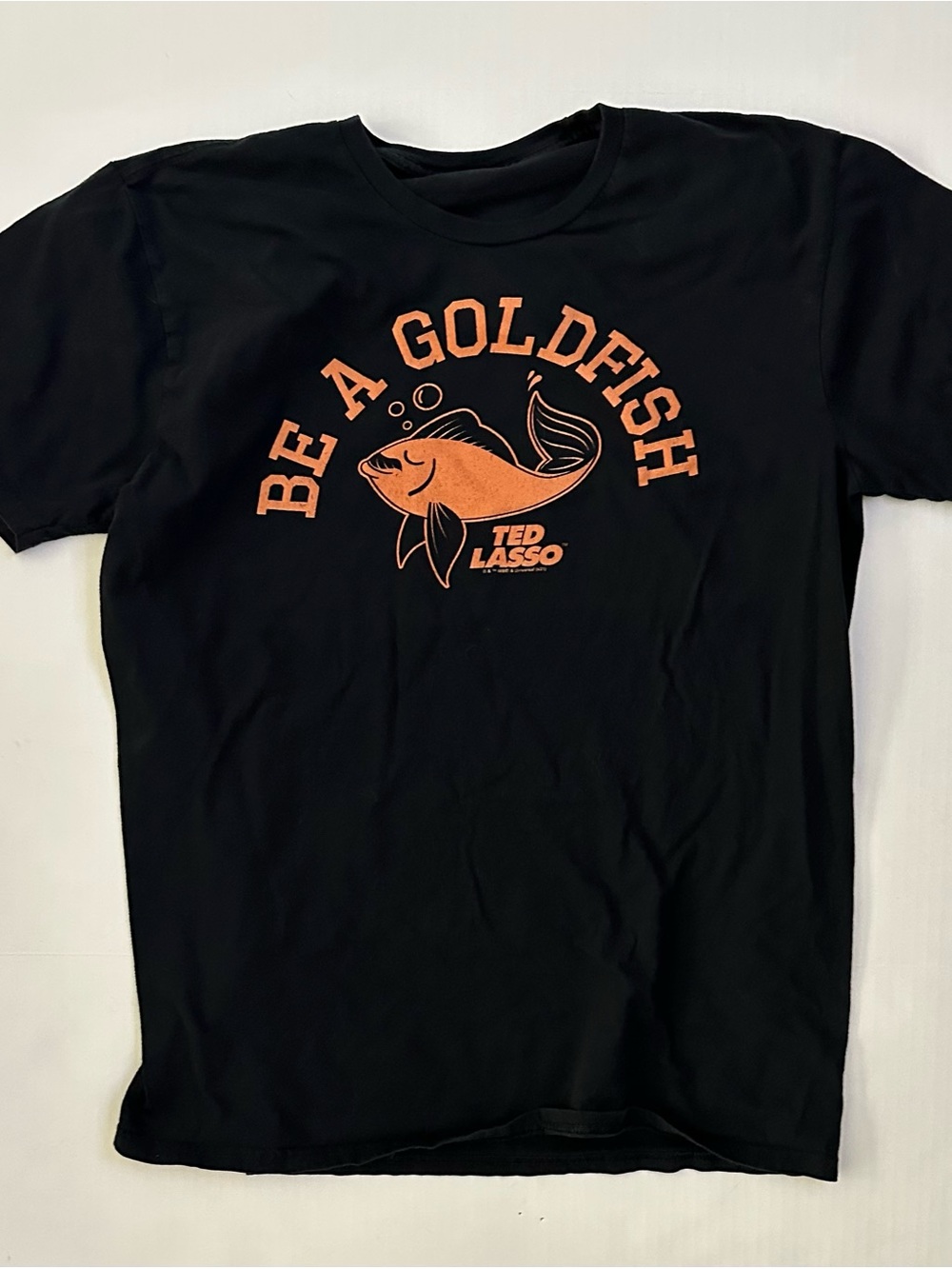 Ted Lasso Black T-Shirt with Orange 'Be A Goldfish' Graphic